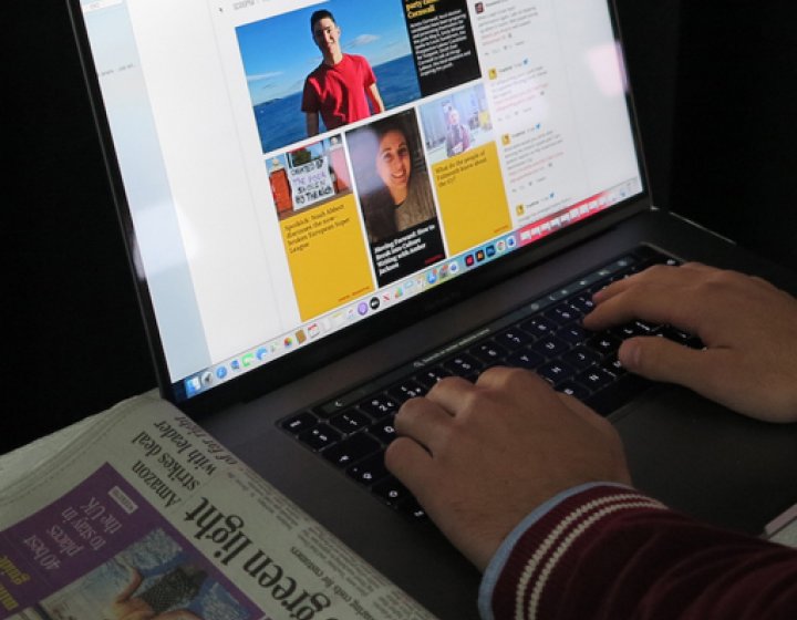 Hands typing on a laptop with a newspaper on a table